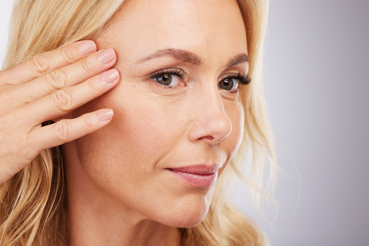 Femme à la peau mature se touchant le visage pour observer les signes du vieillissement de la peau.