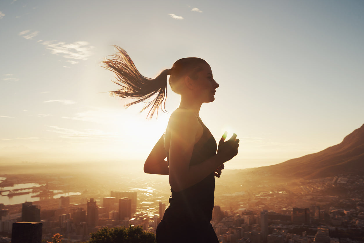 Jeune femme courant au soleil avec en arrière plan la ville.